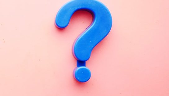 A blue magnet in the shape of a question mark on a pale pink background