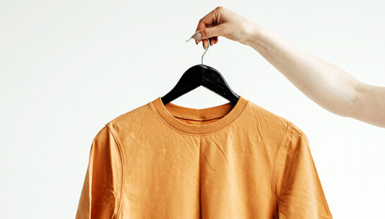 Hand holding a yellow shirt on a clothes hanger