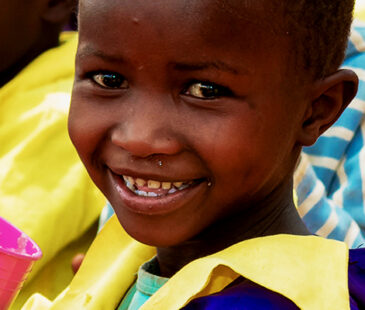 Child in Kenya smiling at camera holding a cup of food