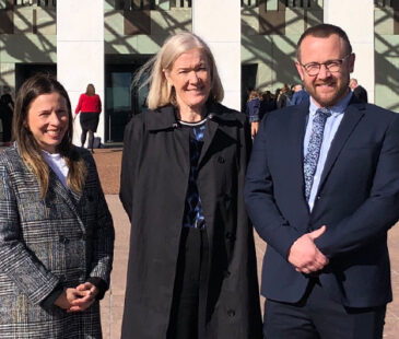 Sarah Knop, Melissa Lipsett and Mike Bartlett standing in front of Parliament House in Canberra