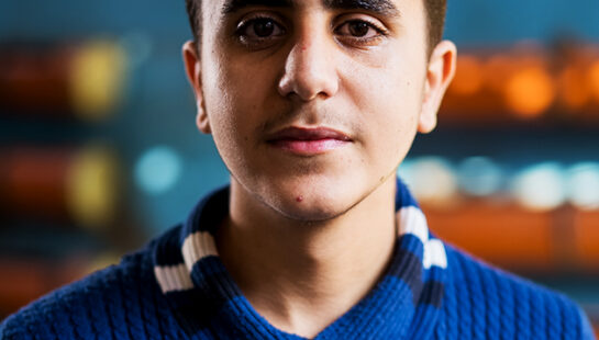 Headshot of boy smiling at camera wearing a blue and cream sweater