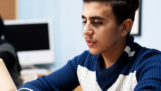 Luay holds a book whilst sitting at a school desk