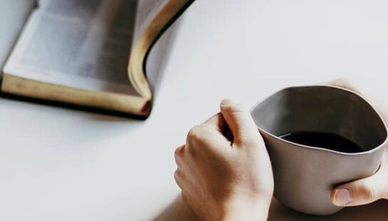 person holding bible and person holding mug of coffee