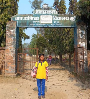 A young girl stands in front of school.