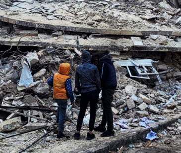 Three boys standing in front of building rubble