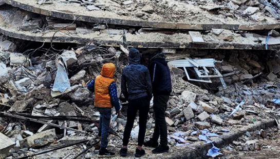 Three boys standing in front of building rubble