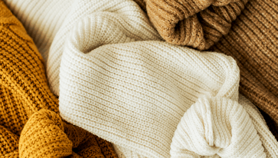 Pile of knitted jumpers in warm coloured tones
