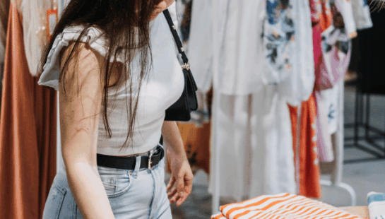 Woman in a shopping centre looking down at a table of folded clothes